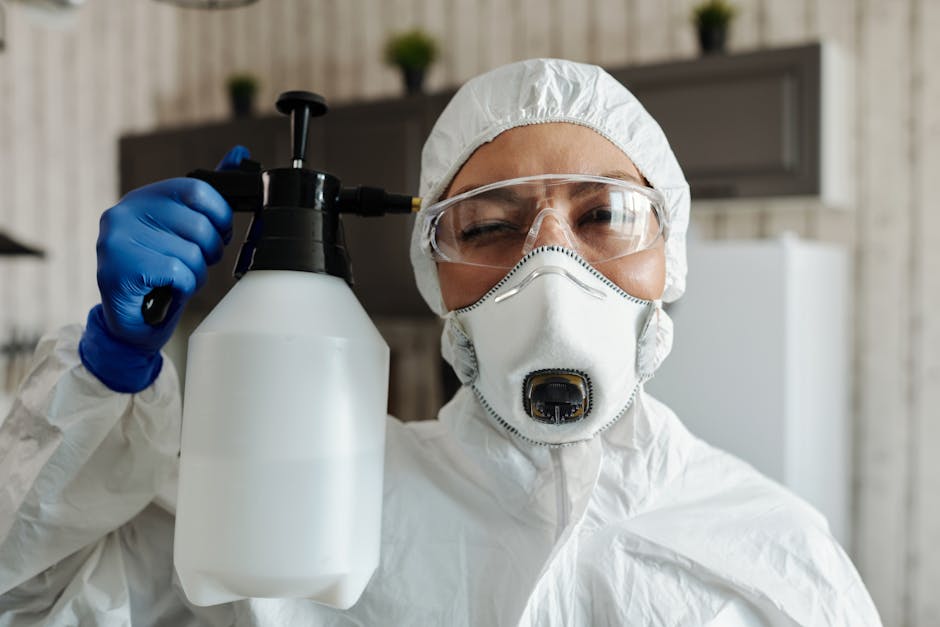 Female wearing protective equipment and spraying disinfectant indoors.